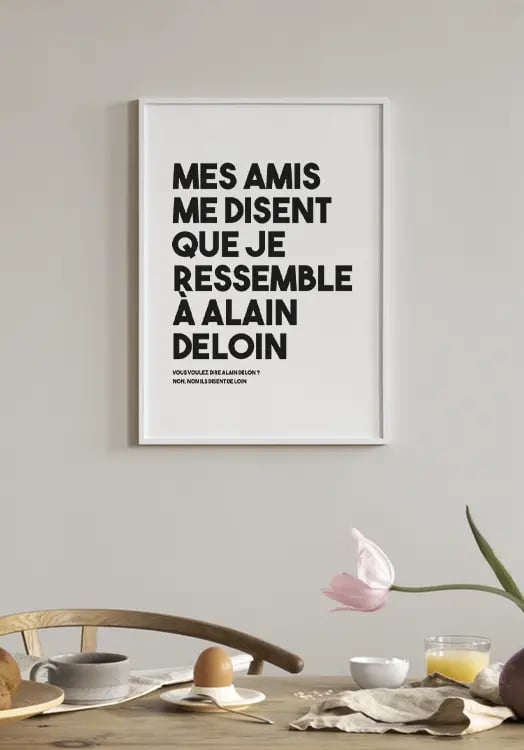 L’affiche Alain Deloin dans un cadre clair, accrochée au-dessus d’une table de petit-déjeuner