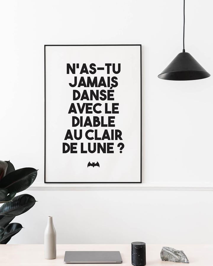 L’affiche du Joker dans un cadre noir, posée sur un bureau blanc près d’une lampe suspendue et d’une plante