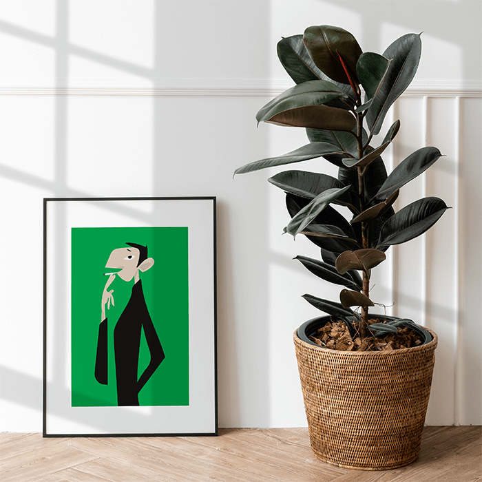 L’affiche Gainsbourg sur fond vert dans un cadre noir à passe-partout blanc, posée sur un parquet près d’un caoutchouc en pot
