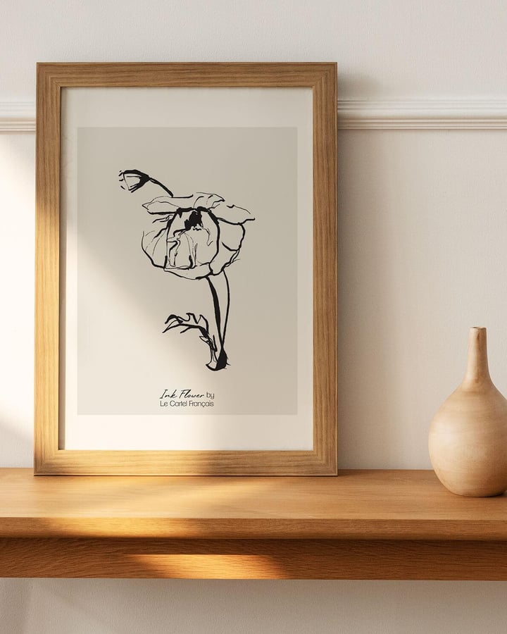 L’affiche Ink Flower No.1 dans un cadre en bois clair à passe-partout, posée sur une étagère près d’un vase beige
