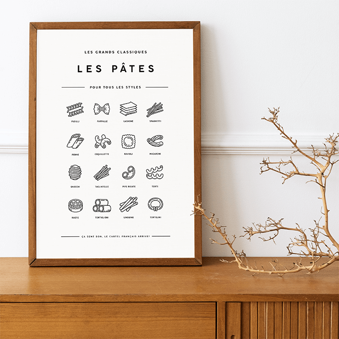 L’affiche Les Pâtes dans un cadre en bois foncé, posée sur un buffet à côté de branches sèches