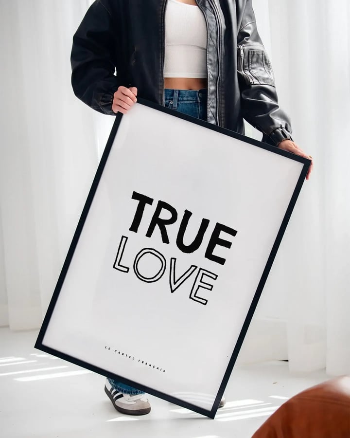 Une personne en veste de cuir tient l’affiche True Love dans un cadre noir