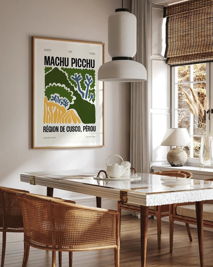 L’affiche Machu Picchu encadrée dans une salle à manger, au-dessus d’une table en marbre et de fauteuils cannés
