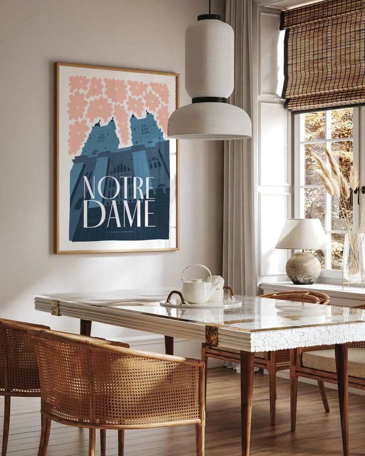 L’affiche Notre-Dame de Paris encadrée dans une salle à manger lumineuse, au-dessus d’une table en marbre et de chaises cannées