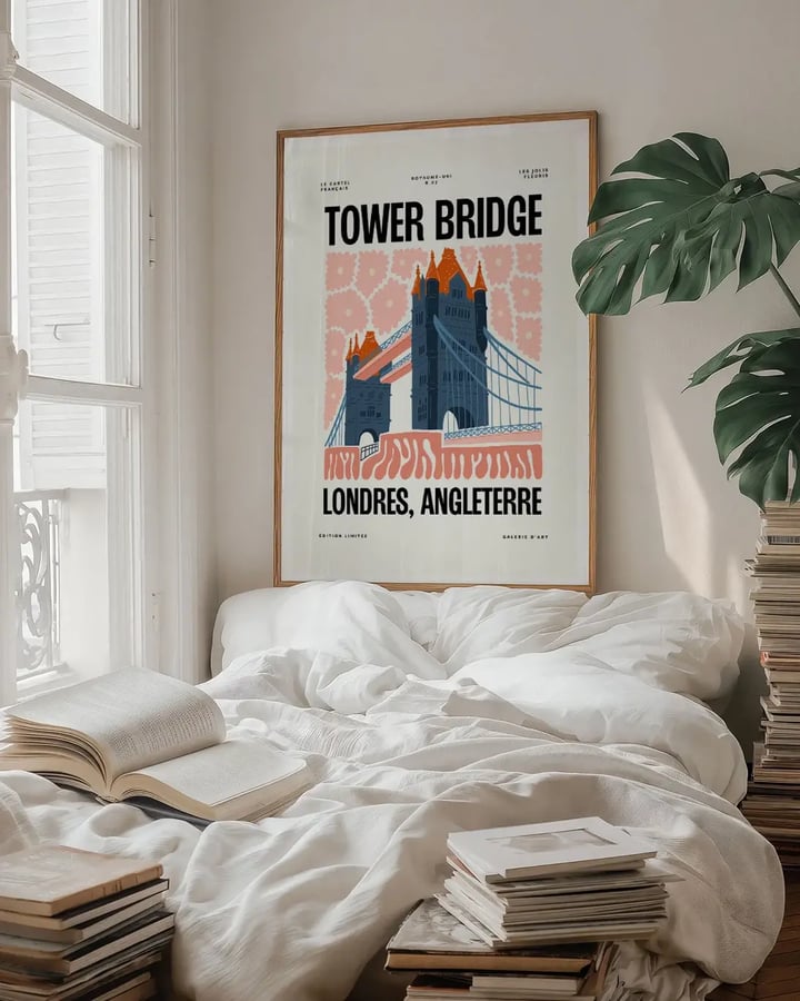 L’affiche Tower Bridge encadrée au-dessus d’un lit, près d’une fenêtre et d’une plante verte, avec des livres empilés