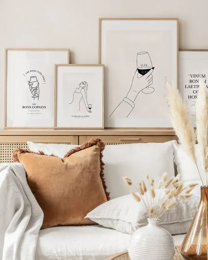 L’affiche Glouglou dans un cadre en bois clair, posée sur un buffet avec d’autres affiches de vin, au-dessus d’un canapé blanc