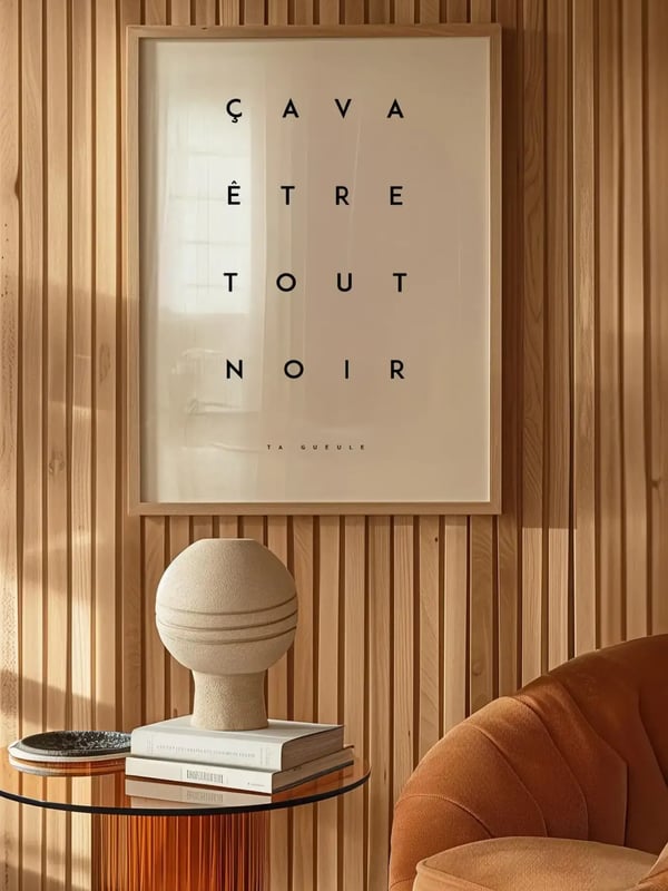 Affiche Ça va être tout noir encadrée sur un mur en lames de bois, au-dessus d’une console