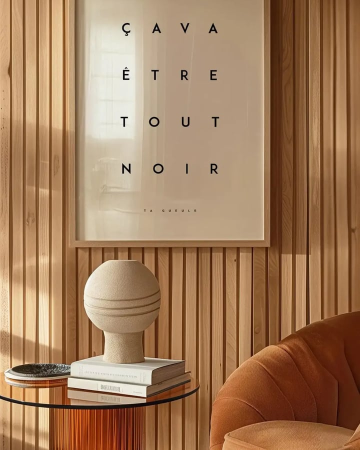 L’affiche Ça va être tout noir dans un cadre en bois clair, au-dessus d’un guéridon devant un mur en lattes de bois