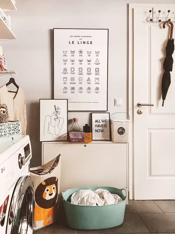 Affiche Le Linge encadrée dans une buanderie, au-dessus d’un panier à linge