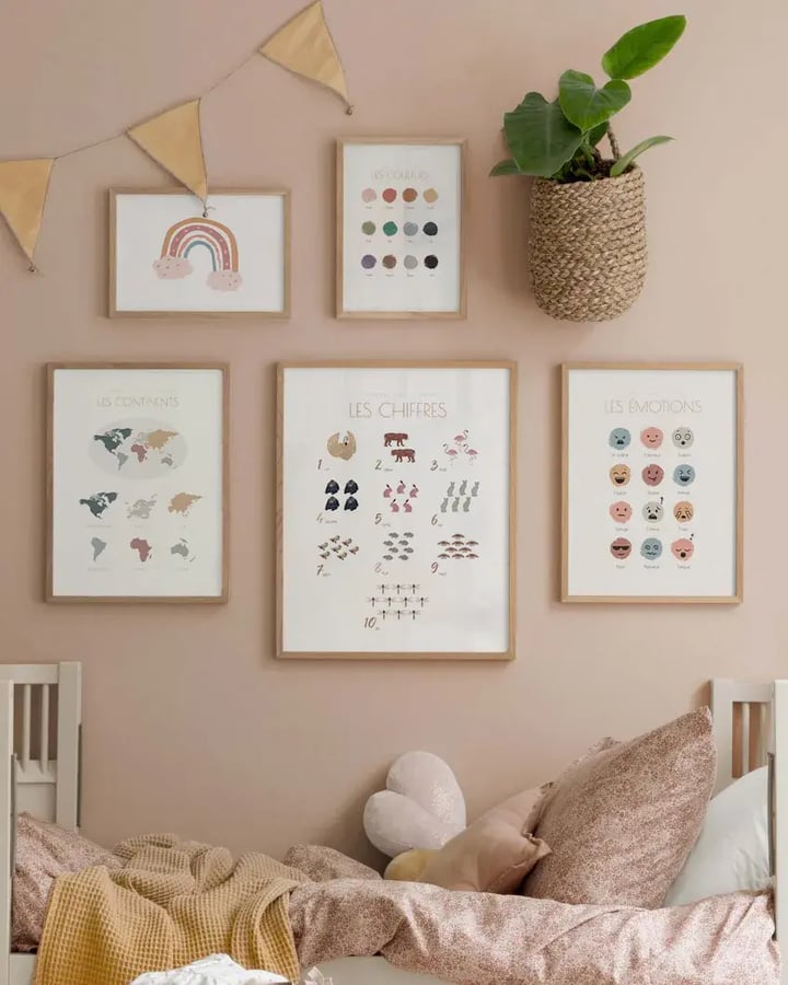 L’affiche Les continents encadrée de bois clair sur le mur rose d’une chambre d’enfant, avec d’autres affiches de la collection