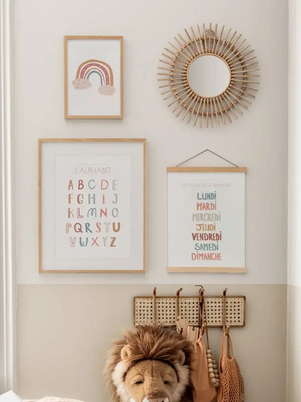 Affiche L’alphabet en couleurs douces dans un cadre en bois, sur le mur d’une chambre d’enfant à côté d’un miroir en rotin