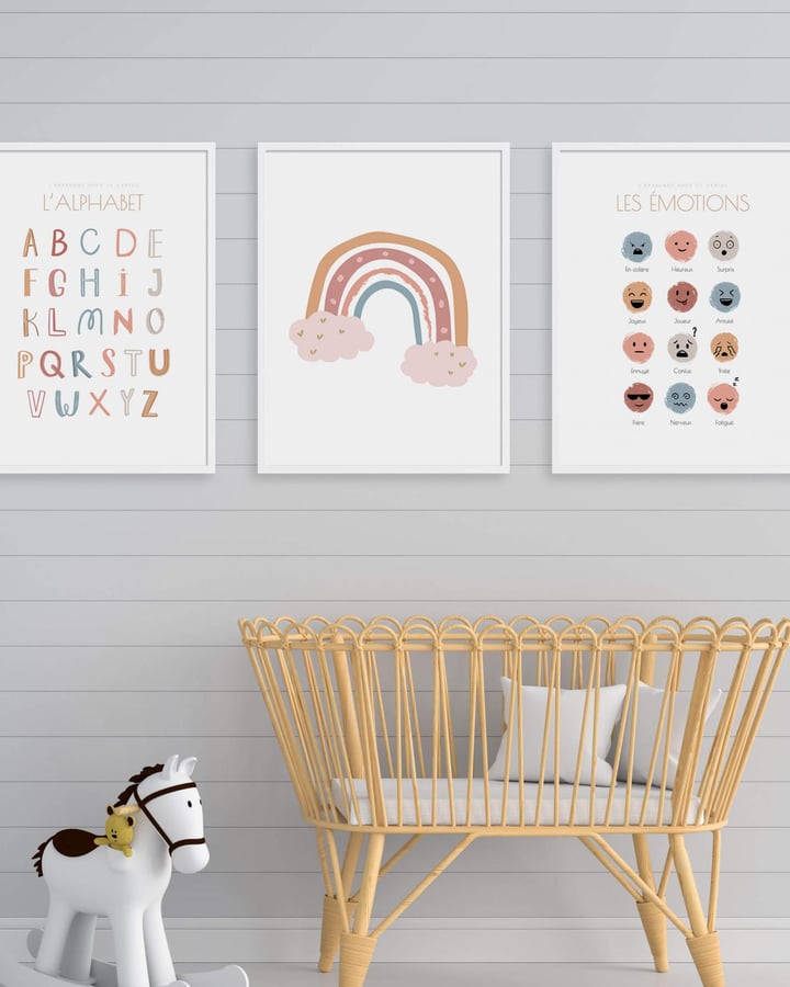 L’affiche Les émotions encadrée de blanc au-dessus d’un berceau en rotin, à côté de L’alphabet et de l’arc-en-ciel