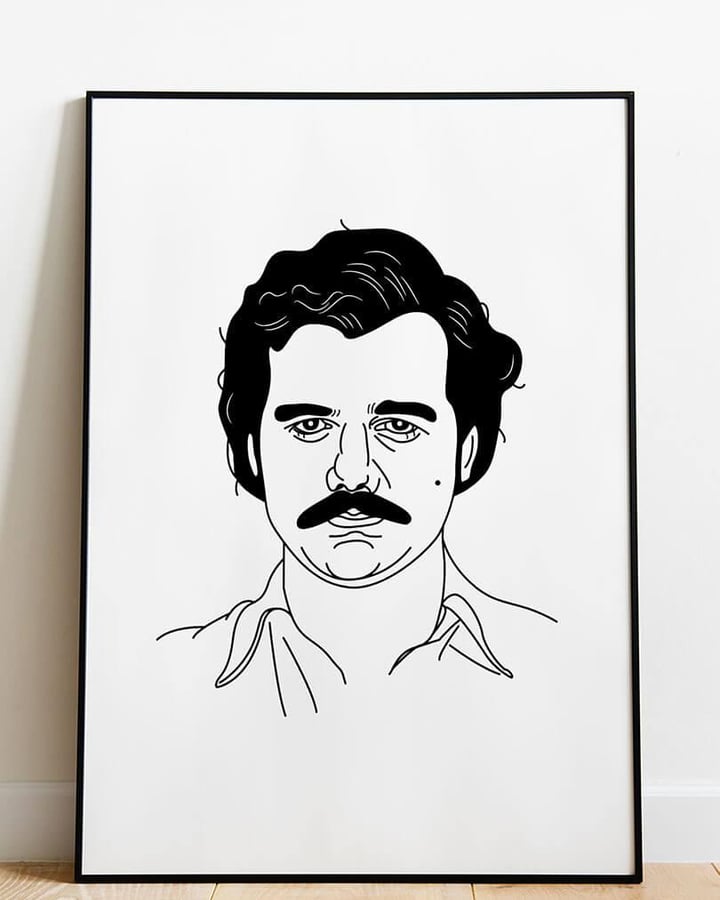 L’affiche Pablo Escobar dans un cadre noir, posée sur un parquet contre un mur blanc