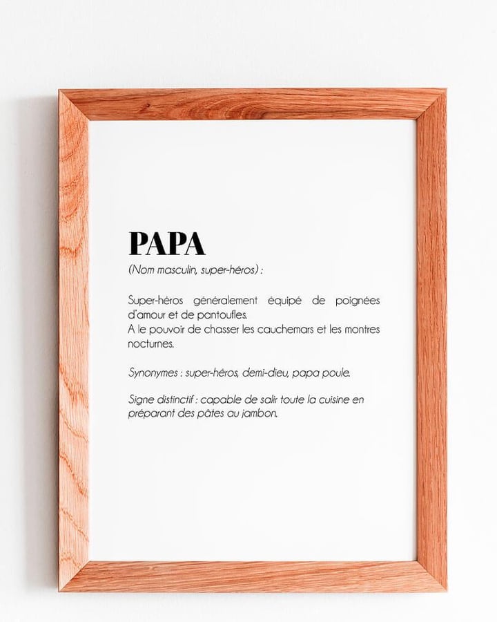 L’affiche Définition Papa poule dans un cadre en bois, accrochée à un mur blanc