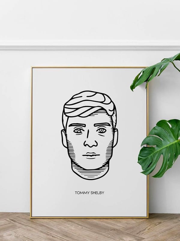 Affiche Tommy Shelby, un portrait au trait noir, dans un cadre doré posé au sol à côté d’une plante
